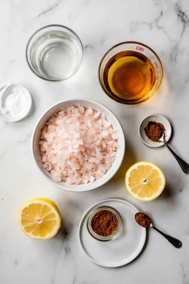 A clear glass of warm water with dissolved pink salt and fresh lemon, photographed in soft morning light on a rustic kitchen counter.