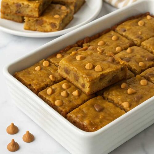 Butterscotch Toffee Cookie Bars in a white baking dish with gooey center and butterscotch chips on a marble countertop