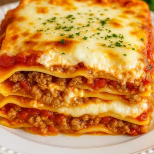 Close-up of million dollar lasagna with melted cheese, meat sauce, and layered noodles on a white plate over a marble table