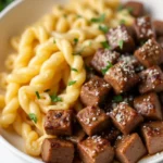 Garlic butter steak bites served over creamy spicy Cajun Alfredo twisted pasta in a white ceramic bowl with fresh parsley on top
