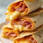 Sliced air fryer chicken ham and cheese wraps stacked on a plate with melted cheese oozing out