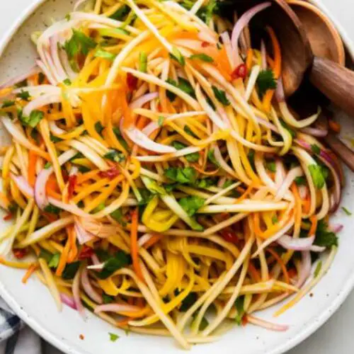 Green mango salad with shredded carrots, onions, and Thai chilies on a white plate