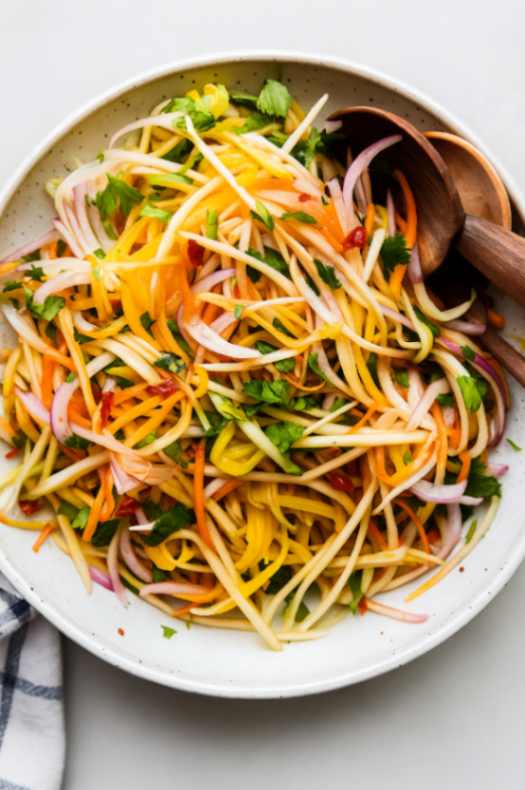 Green mango salad with shredded carrots, onions, and Thai chilies on a white plate