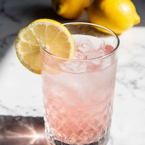 A clear glass of warm water with dissolved pink salt and fresh lemon, photographed in soft morning light on a rustic kitchen counter.