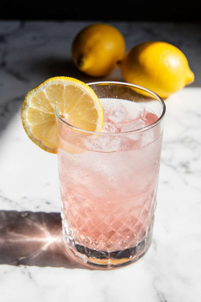 A clear glass of warm water with dissolved pink salt and fresh lemon, photographed in soft morning light on a rustic kitchen counter.
