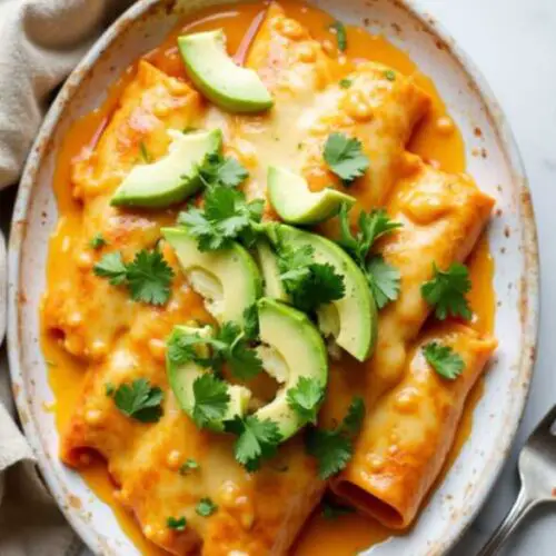 Homemade easy chicken enchiladas served with cheesy sauce, fresh cilantro, and sliced avocado on a marble table
