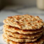 Stack of freshly made oat flatbread on a marble table with avocado and herbs