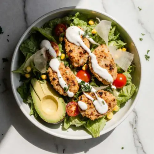 Homemade ranch dressing being poured over a crispy chicken salad.