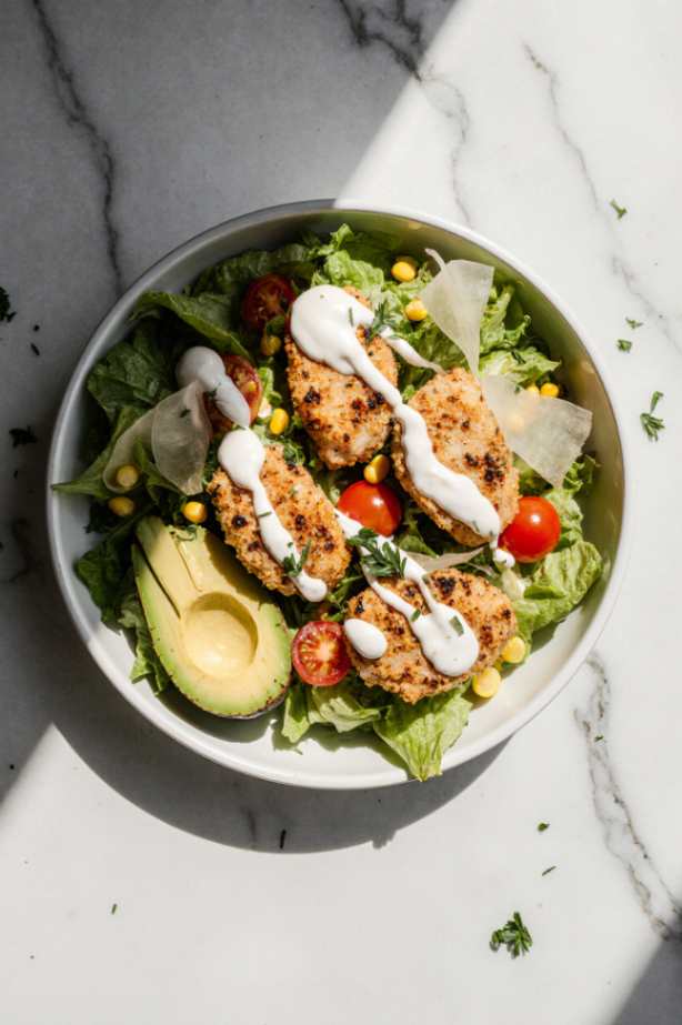 Homemade ranch dressing being poured over a crispy chicken salad.