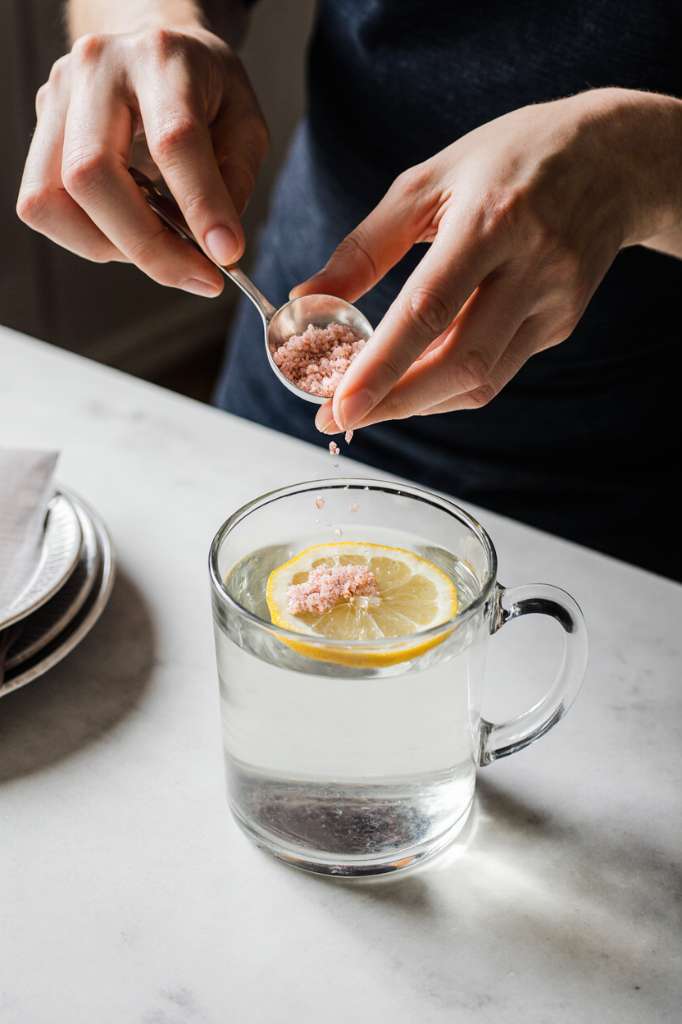 Woman preparing pink salt and lemon water detox drink as part of her natural weight loss morning ritual.
