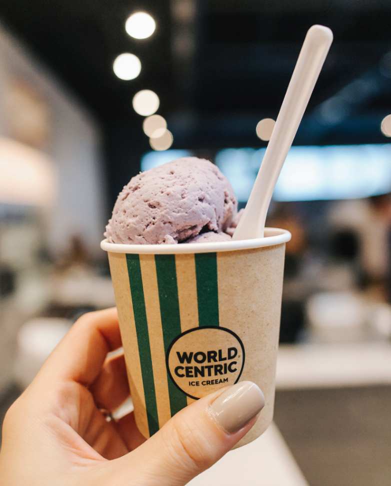 A hand holds a cup of homemade blueberry ice cream with a spoon, showing a safe and delicious gluten-free dessert.