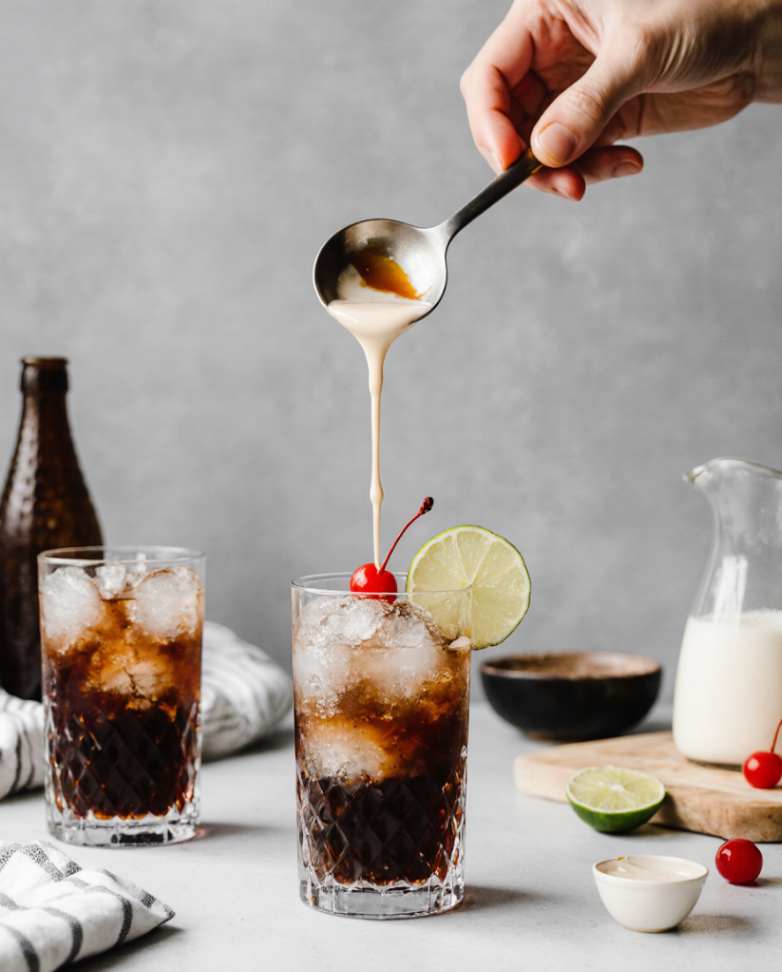 Glass of dirty soda with creamy swirl and garnishes on a rustic table