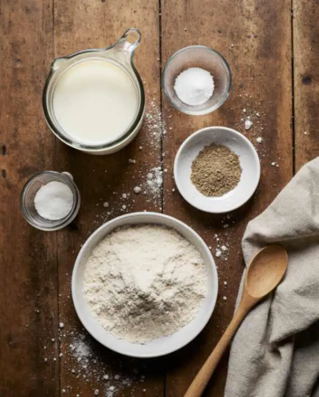 Neapolitan pizza dough ingredients including flour, water, salt, and yeast on a wooden table